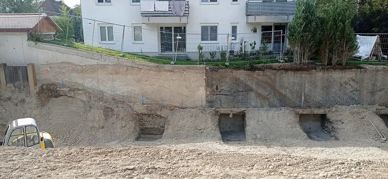 An excavation beside a block of flats with square underpinning pits dug in a row under the foundation