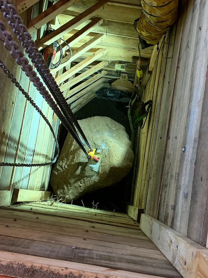 Looking down a deep timber-lined underpinning pit with a boulder being lifted out