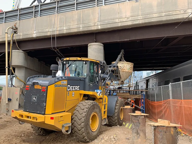 A loader lifting a concrete hopper to pour an underpinning pit under a road bridge